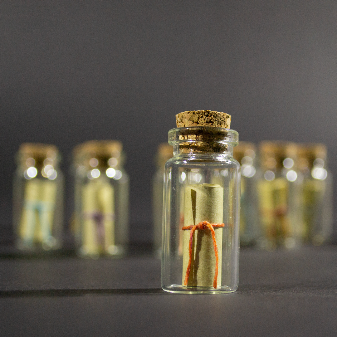 Message in a Bottle product shot with one bottle in focus in the foreground. Inside the bottle is a rolled up scroll.