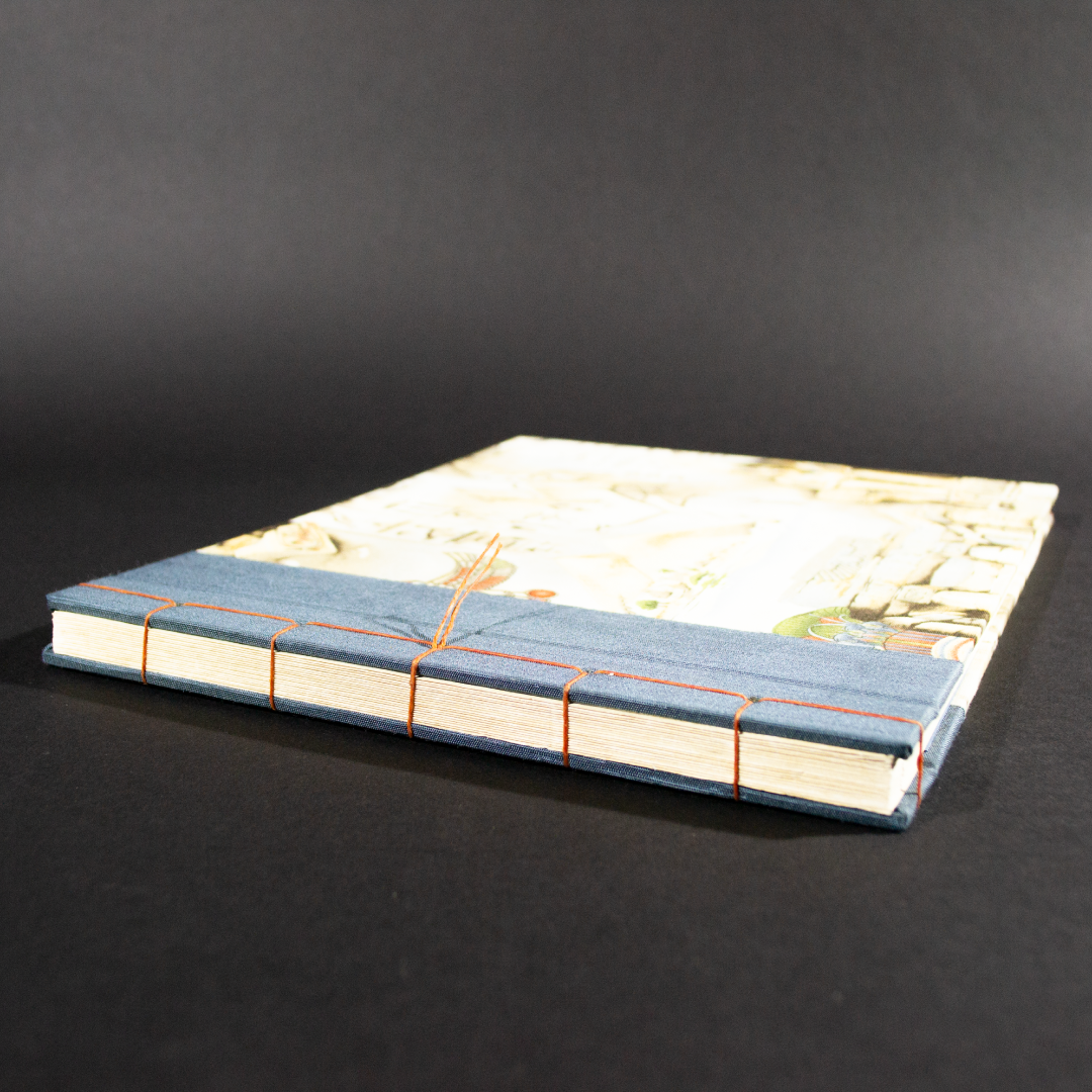 Front cover of stab bound Egyptian photo album showing the blue book cloth left side and a with Egyptian themed fabric featuring a pharaoh, pyramids, and hieroglyphics.
