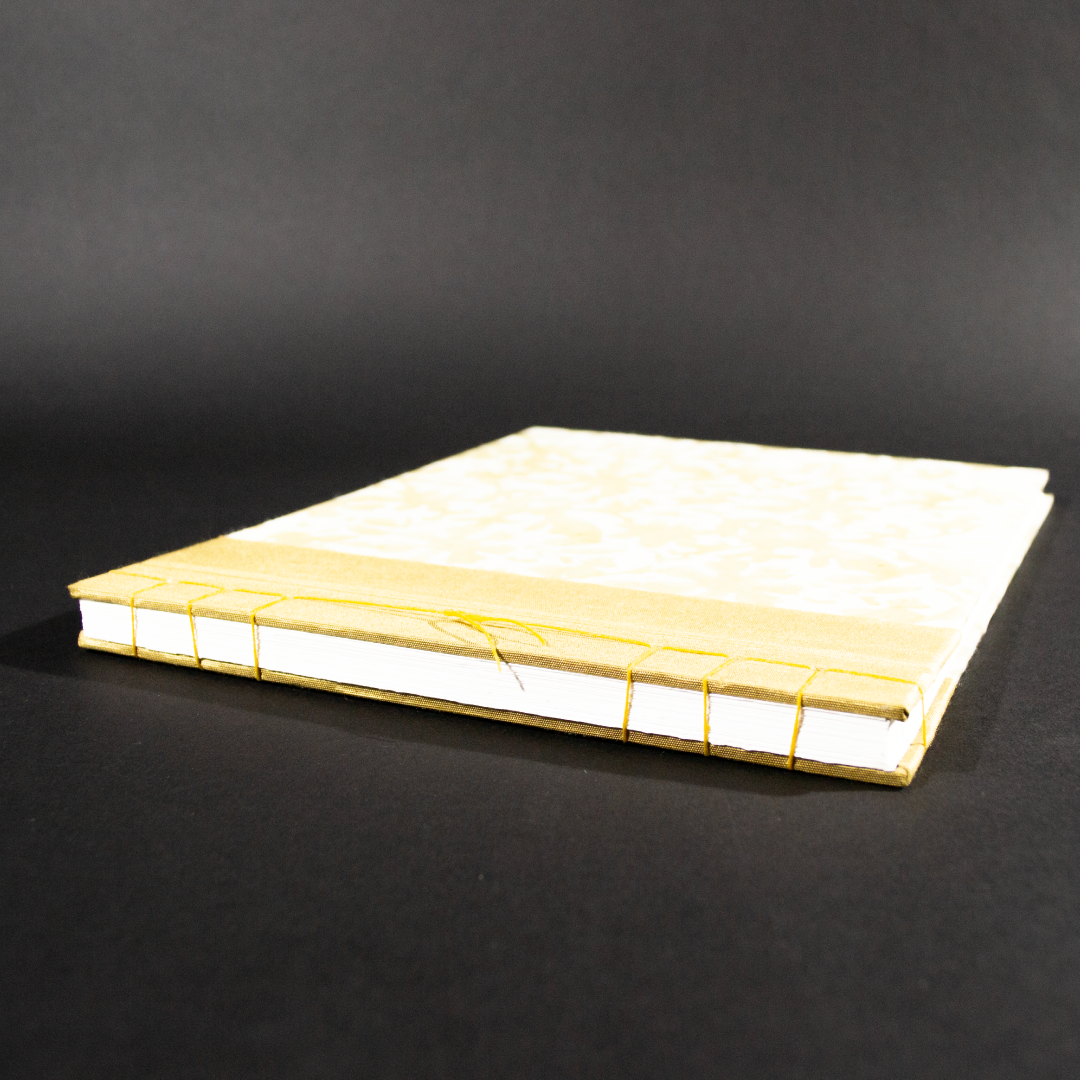 Spine view of this stab bound floral photo album has gold book cloth on the left side and the paper has a waxed floral pattern