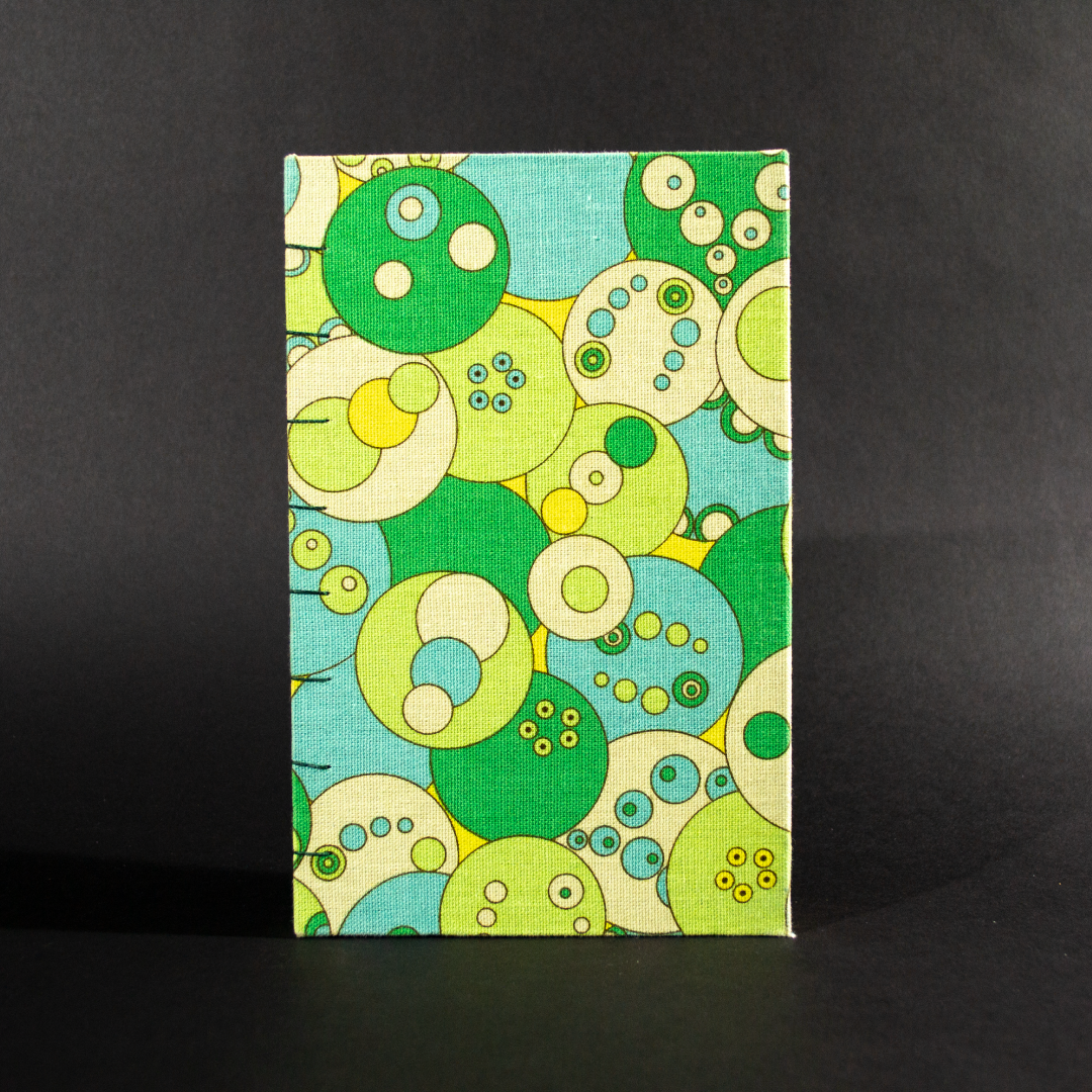The front cover of retro circles quarto Coptic bound journal has overlapping circles in shades of ivory, blue, and green